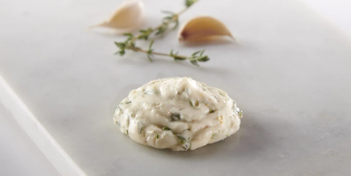 Single garlic herb butter dollop beside garlic cloves and a thyme sprig