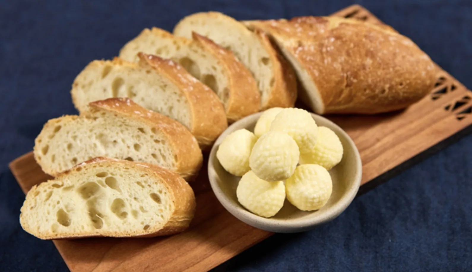 Sliced bread loaf beside a bowl of textured butter balls on a wood board