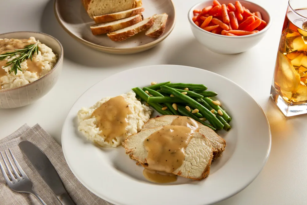 Turkey dinner plate with gravy on a table set with bread, carrots, iced tea and cutlery