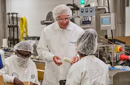 Man in a lab coat speaking with two employees on the production floor