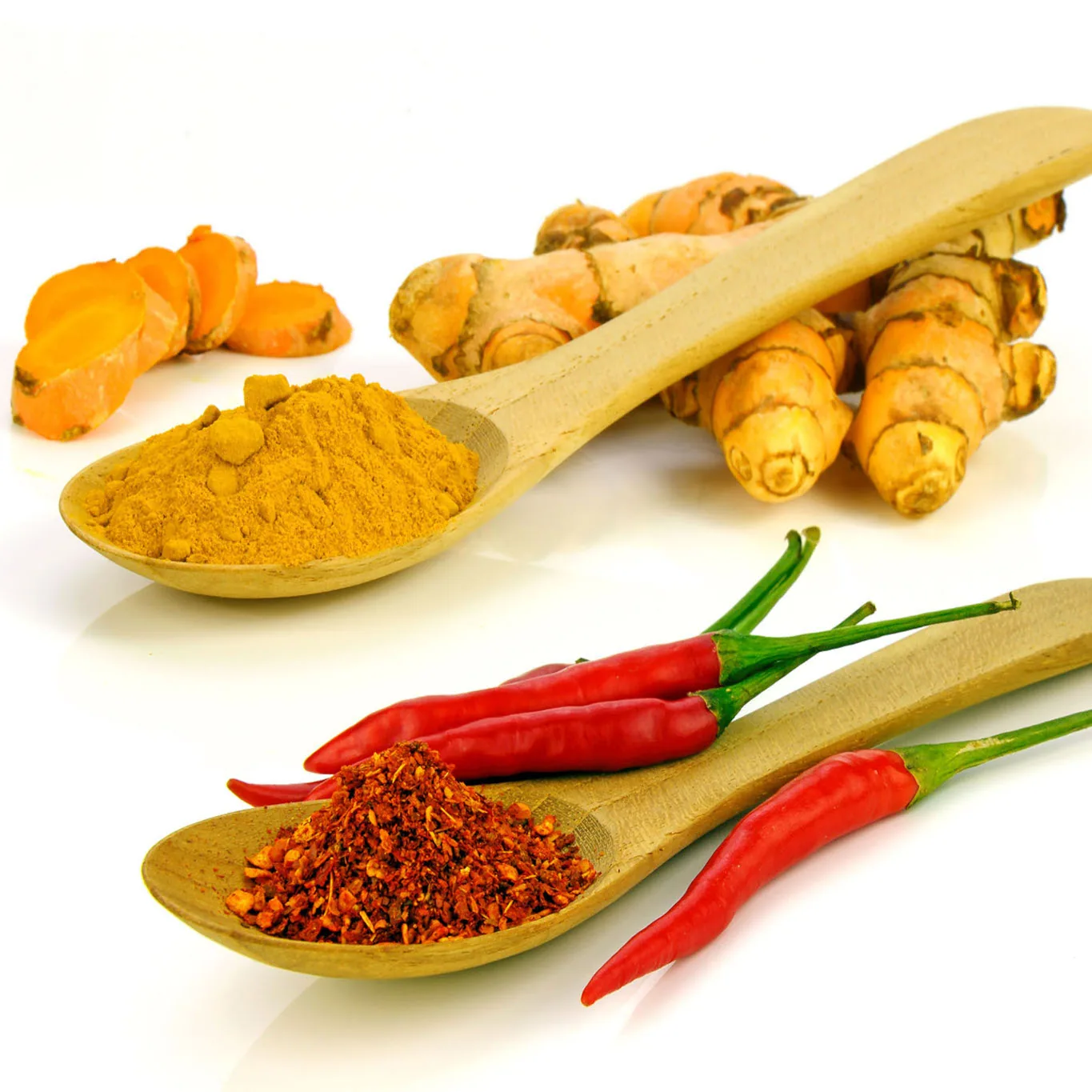 Turmeric powder and root with red chilies on wooden spoons