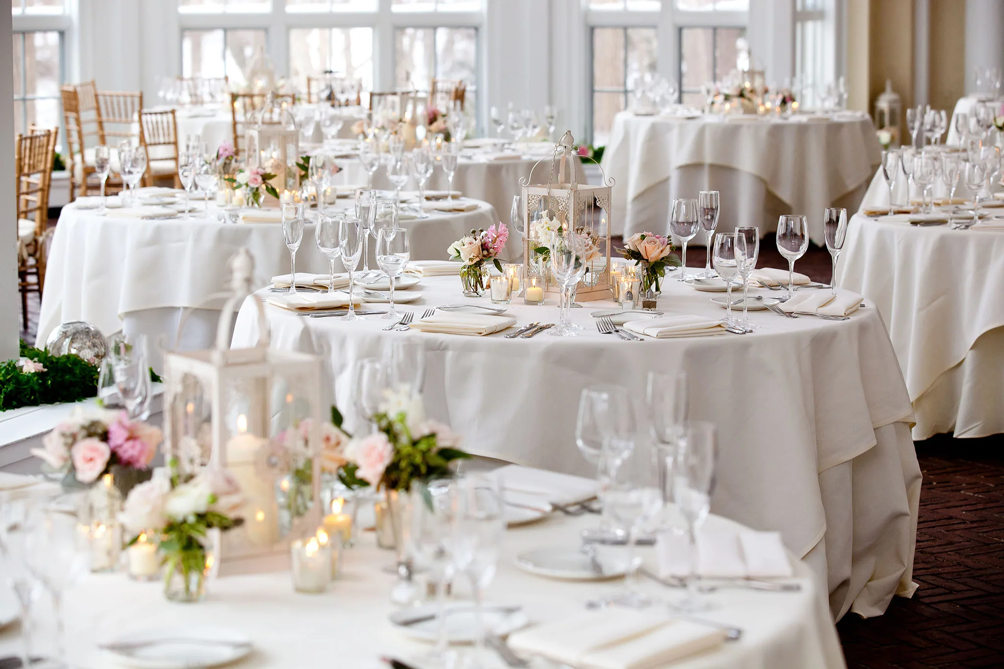 Wedding reception room with round tables set in white linens and candle lanterns