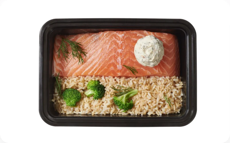 A meal kit tray of salmon, rice and broccoli finished with a flavored butter dollop