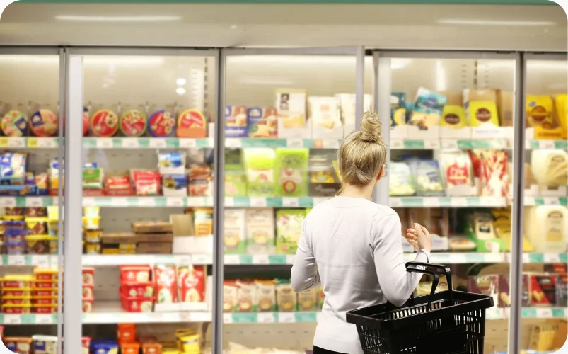 A shopper choosing from a refrigerated case of packaged prepared meals