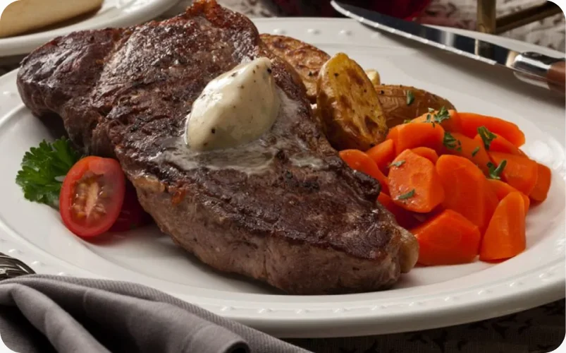 A grilled steak finished with a melting flavored butter dollop, served with carrots and tomato